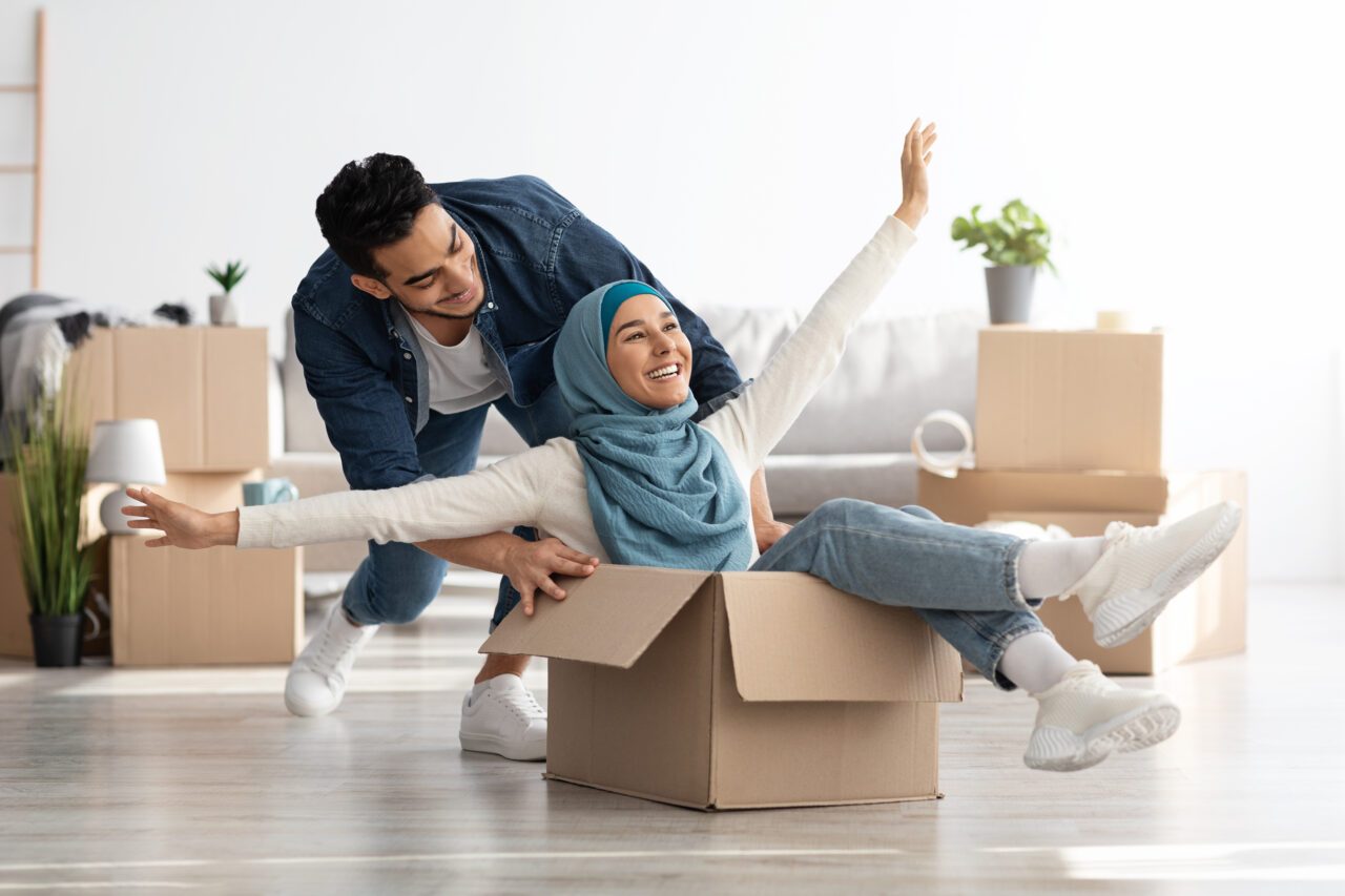 Man pushing a happy woman in a hijab around in a moving box